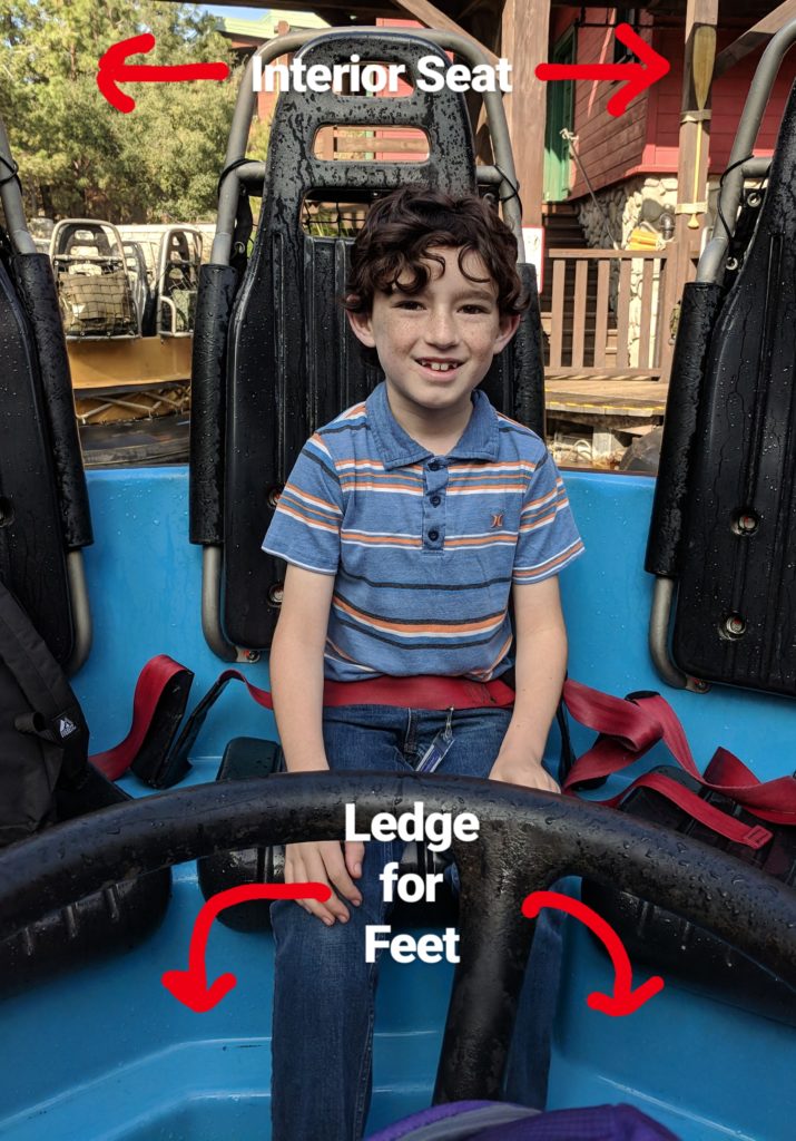 Boy sitting in a raft on Grizzly River Run at Disney California Adventure. Writing indicates that he is in an interior seat and there is a ledge along the floor for him to prop his feet during the ride.